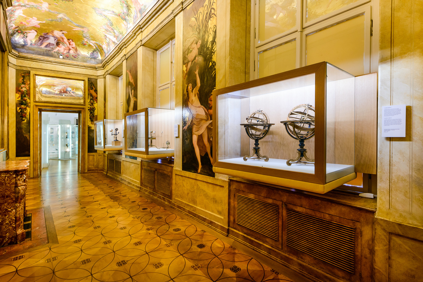 Foto eines schmalen Raums mit prunkvoll verzierten, goldenen Wänden und Glasvitrinen mit Globen