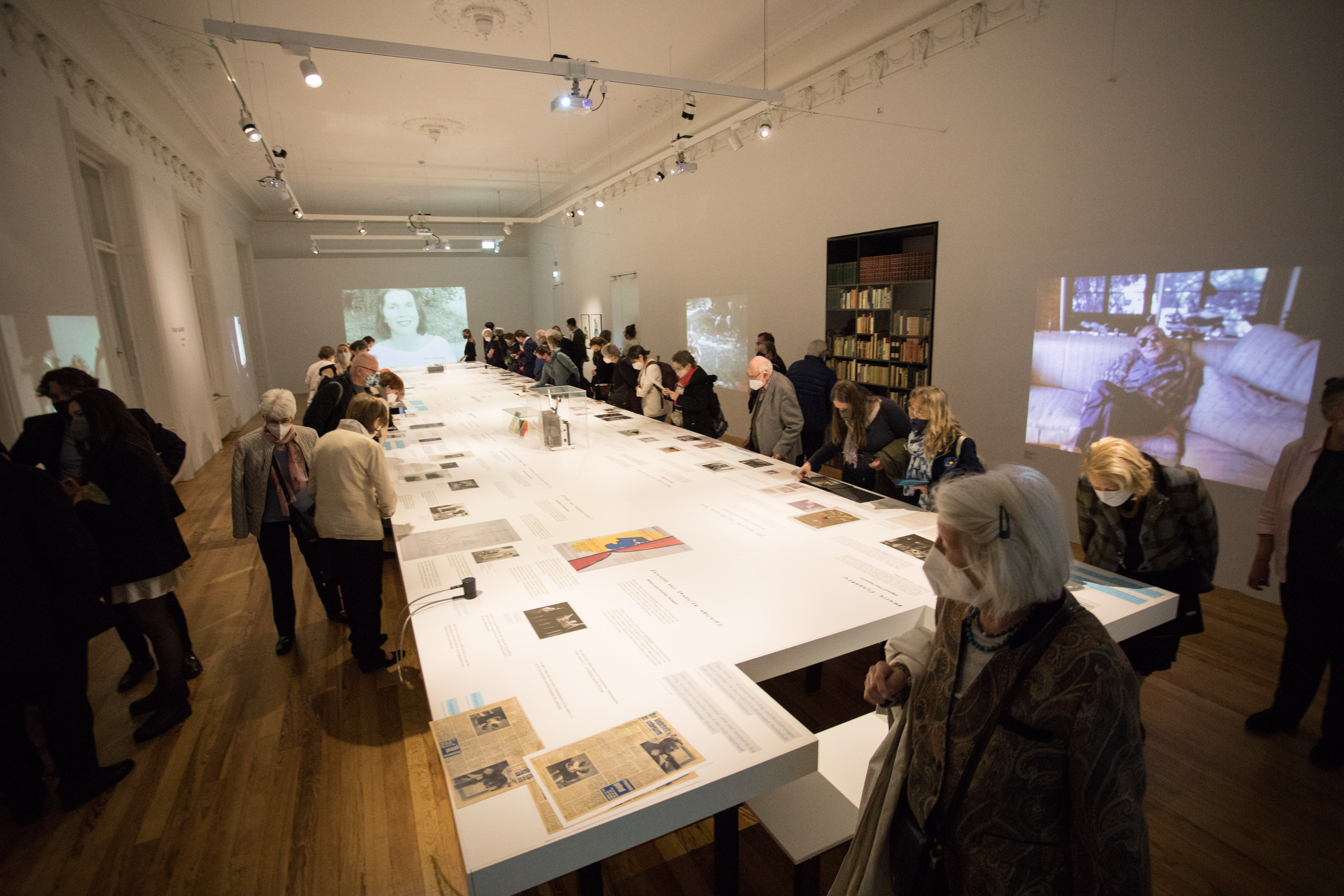 Blick in die Ausstellung mit zahlreichen Besucher:innen, in der Raummitte ein großer Tisch